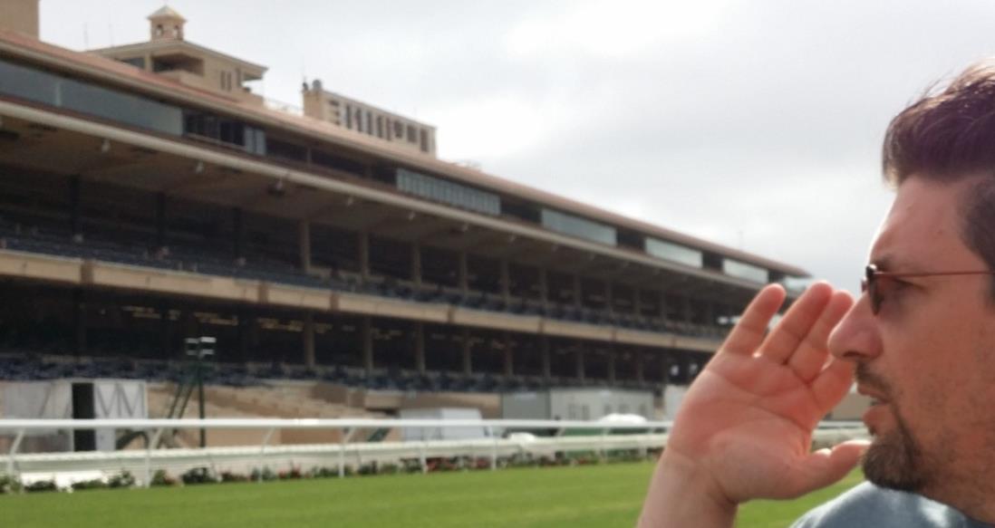 A racing enthusiast at the track, with the grandstand visible in the background